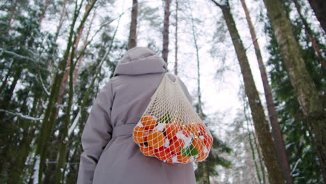 woman with oranges in a net bag in a snowy forest