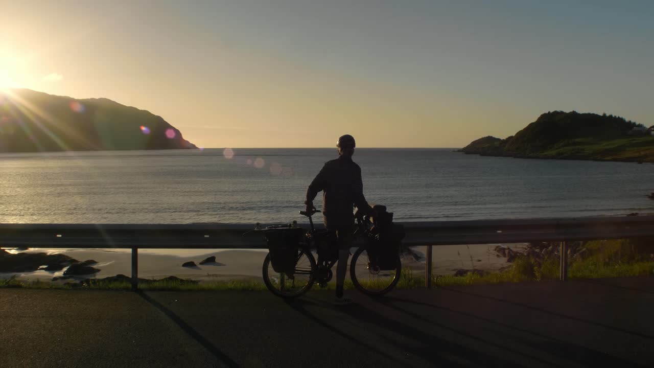 석양에 완전히 포장된 자전거와 함께 beautifull veiwpoint에 도착하는 젊은 남성