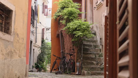 Una-Antigua-Calle-En-Medio-De-Piran-Con-Flores-Y-Una-Bicicleta-Estacionada-Debajo-De-Las-Escaleras