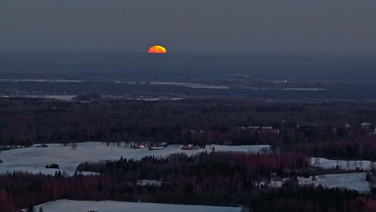 Rød måne hænger lavt over frossent terræn under en stille vinteraften, nedstigning fra luften