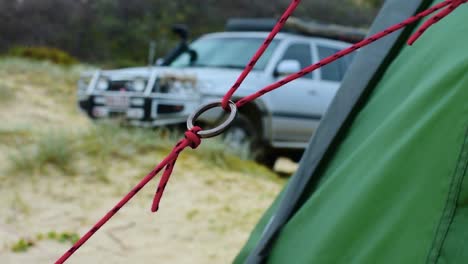 Bonita-Toma-Abstracta-Que-Muestra-Un-Primer-Plano-De-Un-Anillo-De-Metal-En-Una-Cuerda-De-Carpa-En-Un-Campamento-De-Playa,-Con-Un-Hermoso-Campo-De-Profundidad-Y-Un-Camión-4x4-En-Bokeh-En-El-Fondo