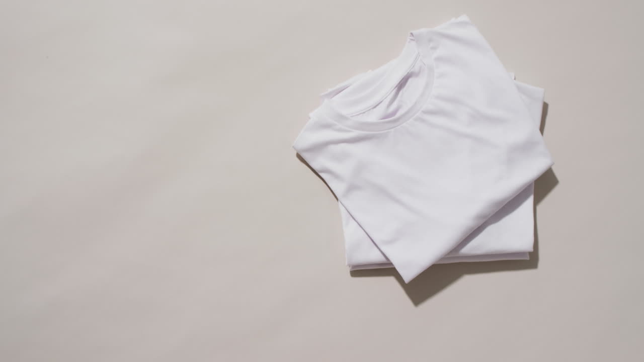 Video of stack of folded white t shirts with copy space on white background