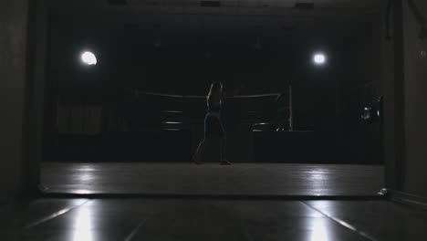 professional beautiful female boxer otbryvatyvat blows conducting a fight with a shadow in a dark hall of the hall in slow motion in blue clothes and red bandages on her wrists. zoom camera. steadicam shot