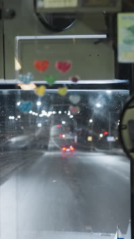 inside view of a car driving on a highway at night, showcasing the illuminated dashboard, rearview mirror reflections, and city lights outside, with other cars on motion