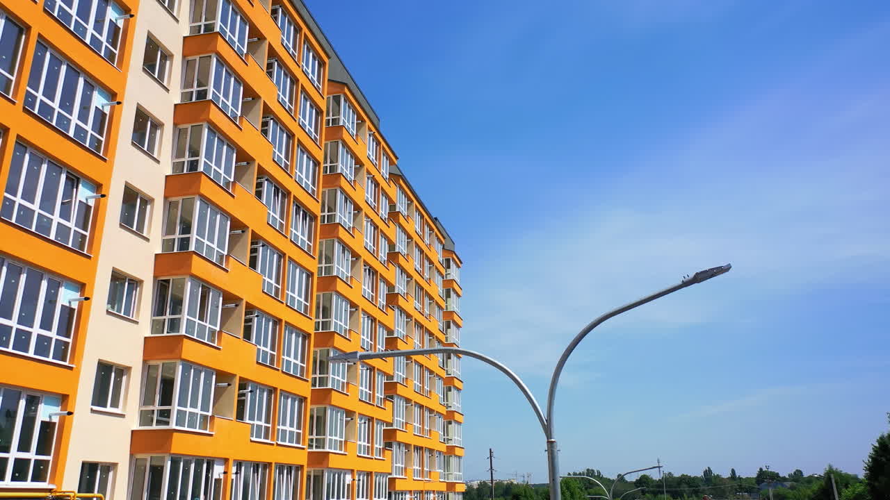 Modern skyscraper of bright color. New multi storey building in the city. Side view of contemporary high-rise against blue sky background.