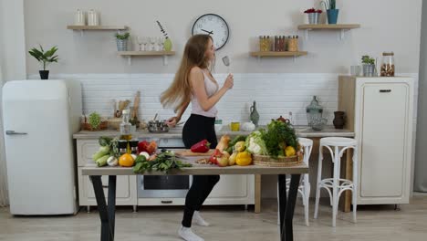 happy vegan girl with slim waist dancing, singing in kitchen. raw vegetable nutrition diet concept