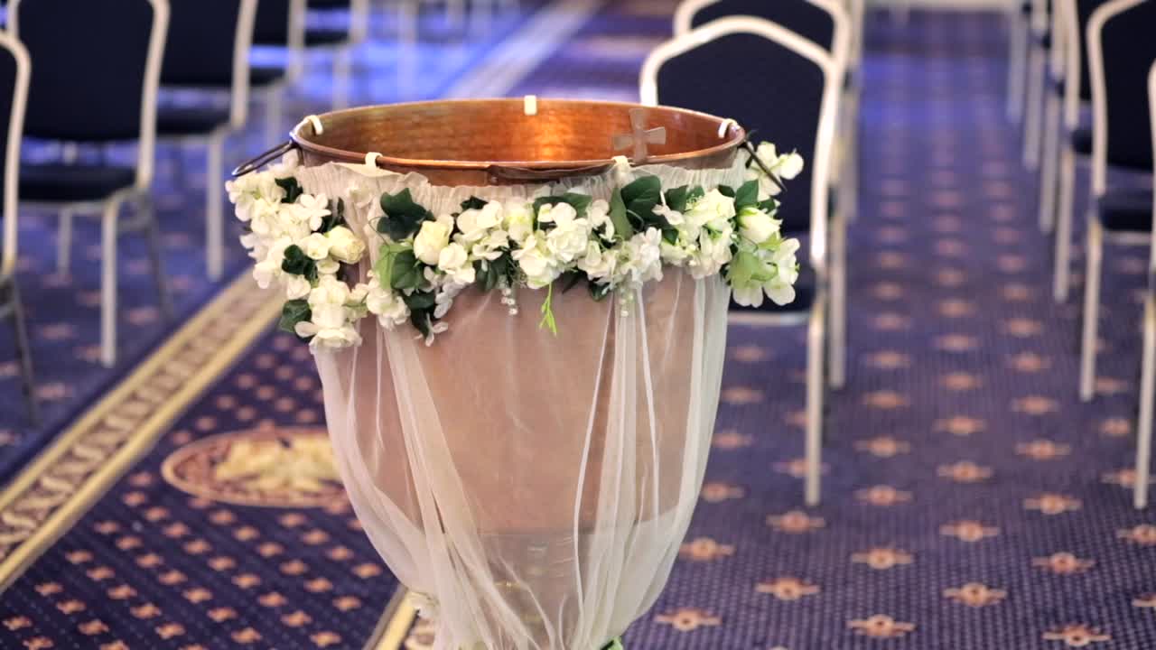 Left-to-right sliding shot of floral baptism font, wooden foreground blurred in view.