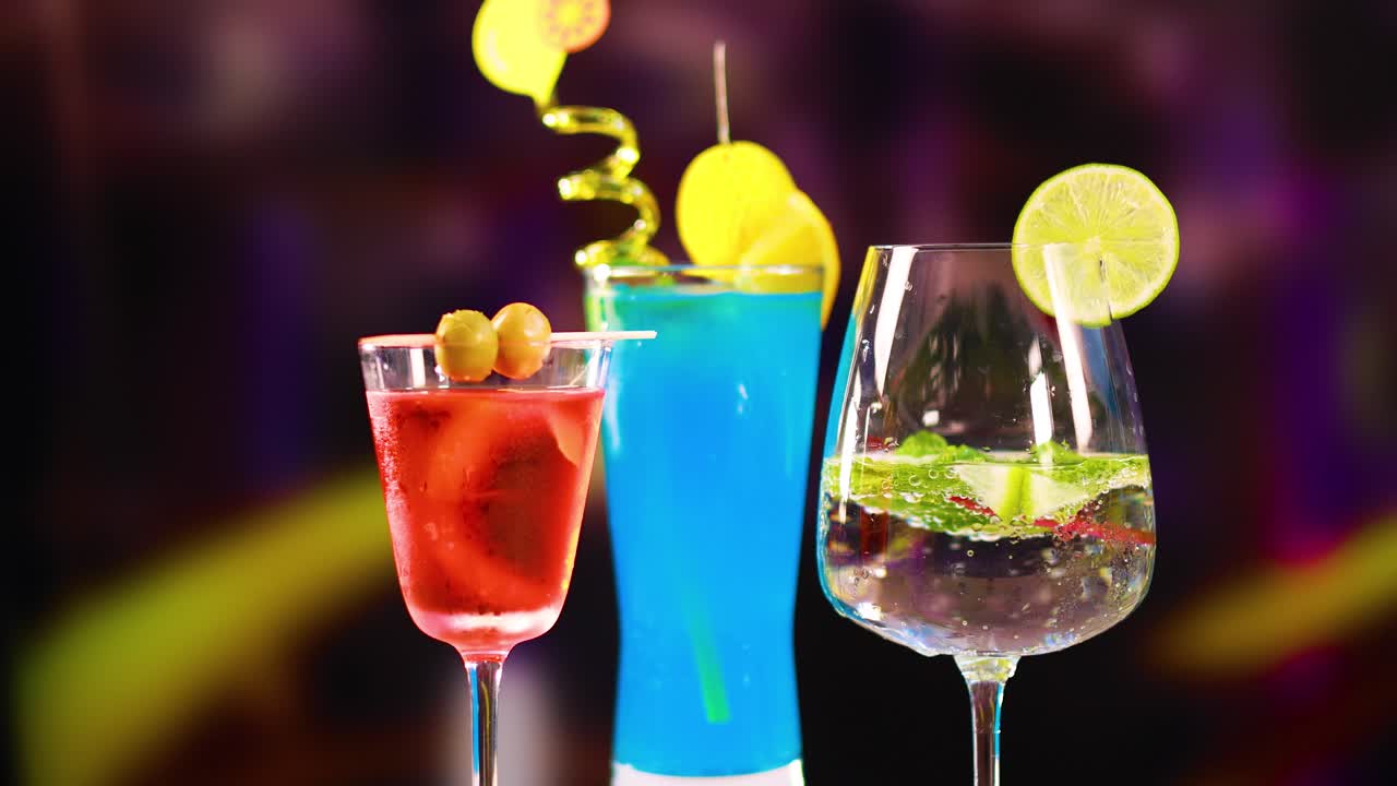 Three colorful cocktails with garnishes in a lively setting. Bright lighting enhances the vivid colors and festive atmosphere