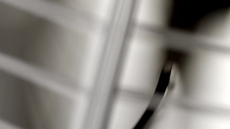 White oscillating fan blades move behind a blurred grille in soft indoor light.