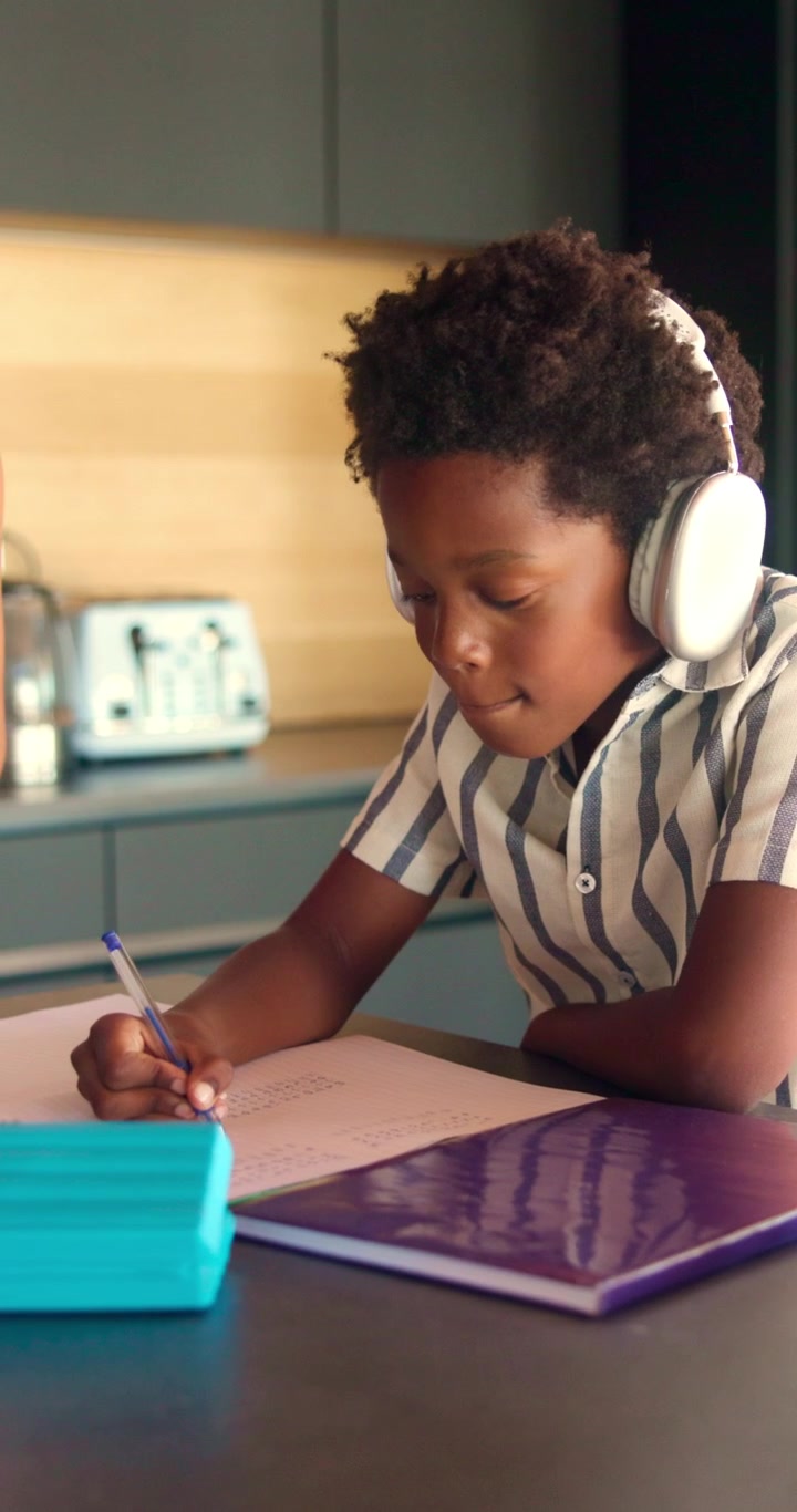 Young Boy Wearing Headphones Writing in a Notebook at Home