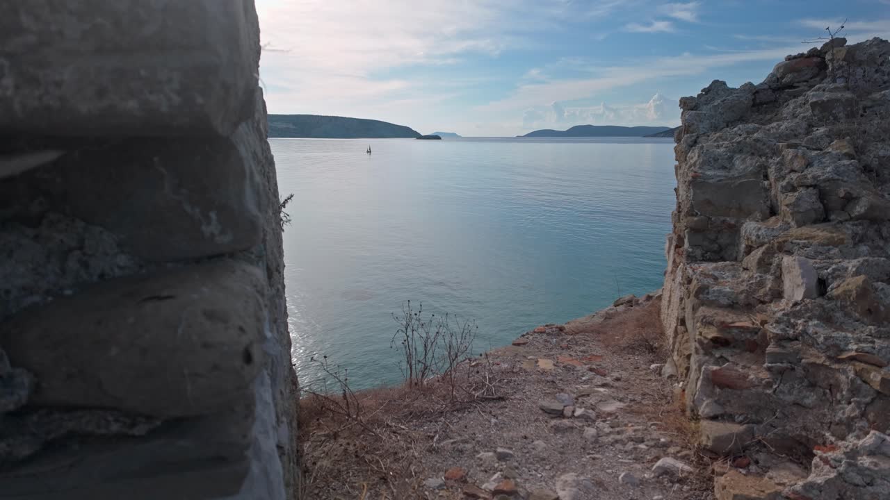 Barca da pesca solitaria in mare calmo al largo di un'isola greca, con vista sui bastioni del castello.
