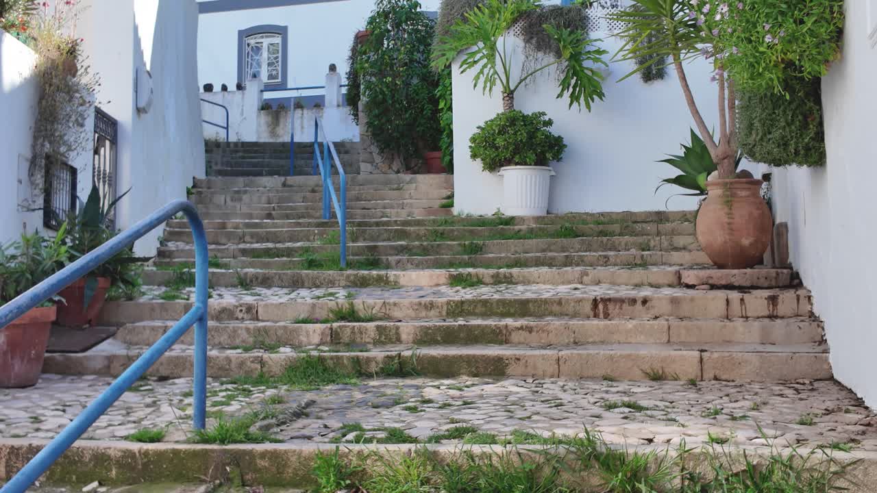 Winding stone stairway ascending towards charming white houses adorned with lush plants and trees in picturesque Ferragudo, Portugal