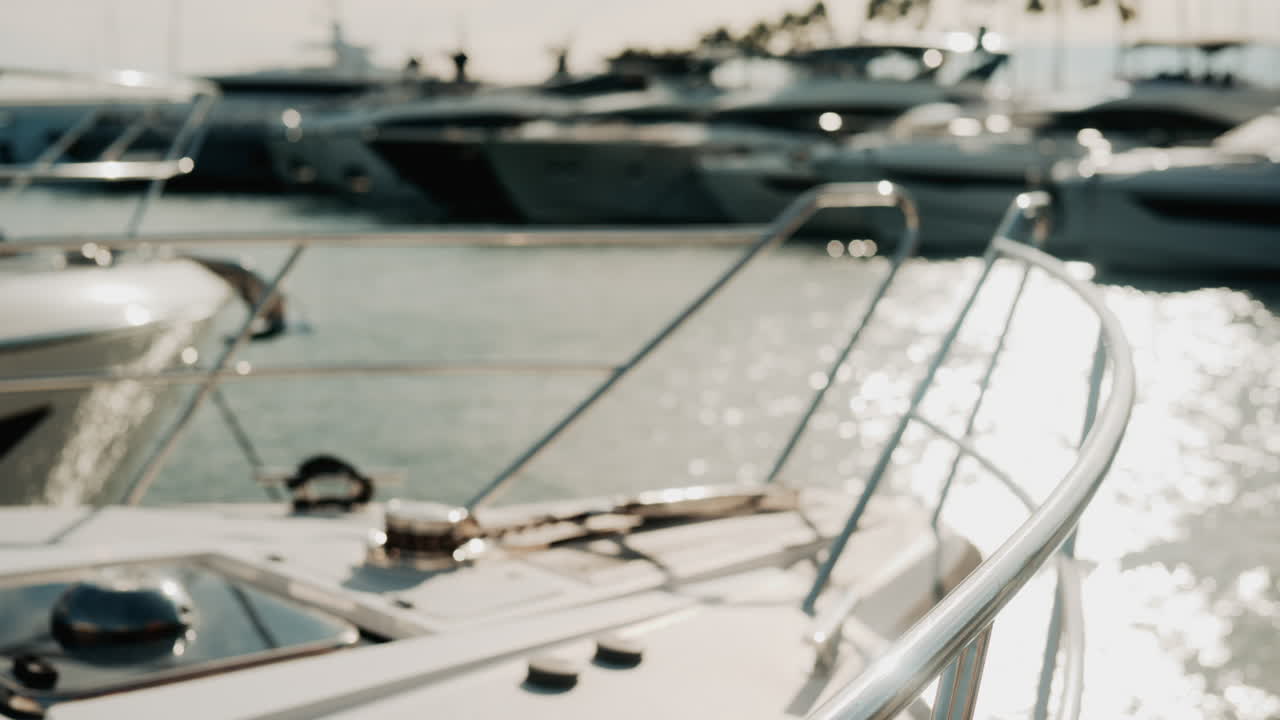 Close up of chrome railing and wooden deck of a luxury yacht docked in a marina under golden light