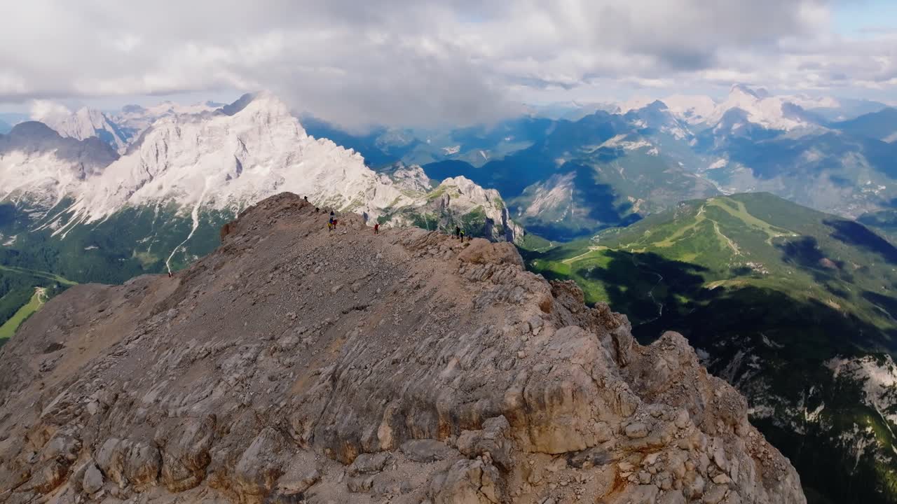toma aérea en órbita que muestra a un grupo de excursionistas que alcanzan la cumbre de la montaña en un sendero estrecho en verano - espectacular toma de drones que muestra la cordillera en dolomitas, italia