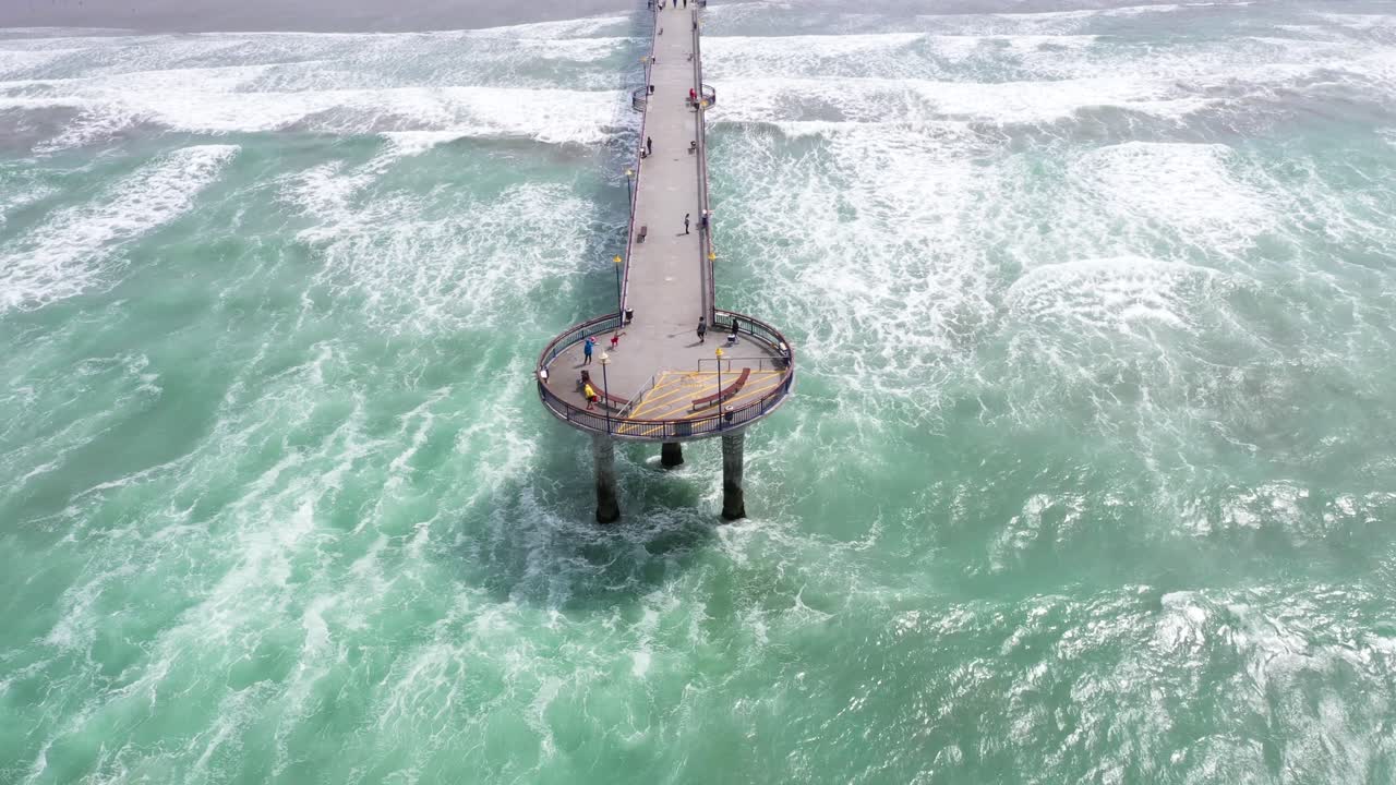 Drone shot revealing pier with fly over down the length of it, township in background.