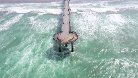 drone shot revealing pier with fly over down the length of it, township in background.