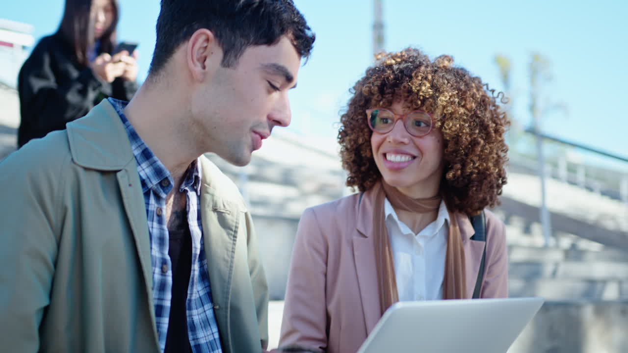 Young Coworkers Sitting with Laptop and Talking Outdoors