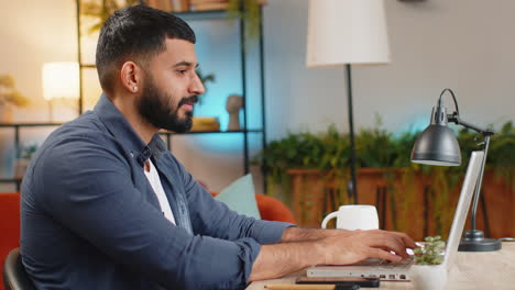 happy arabian man freelancer typing working on laptop writing important email from home office