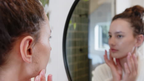 looking in mirror, woman touching face and examining skin in bathroom