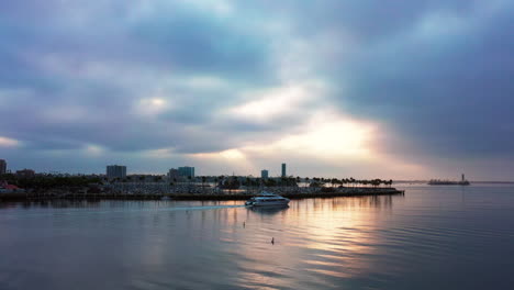 A-luxury-yacht-sailing-through-the-Long-Beach,-California-harbor-at-sunrise-with-the-sunrise-reflecting-off-the-glassy-water