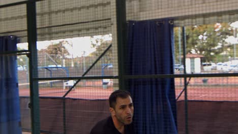 man playing in a padel match swings and hits the ball to the other side of the court