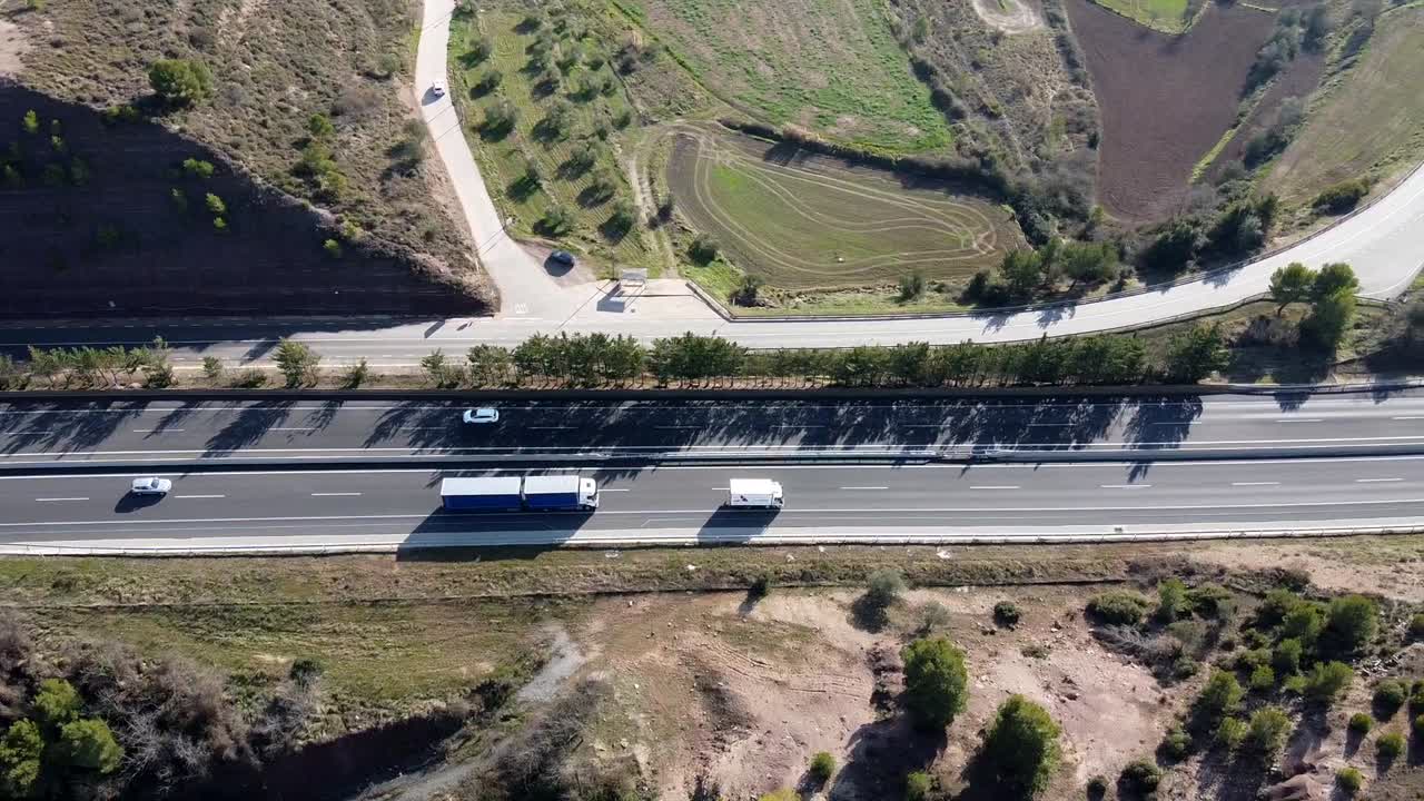 Vista aérea de um caminhão e uma van dirigindo em uma estrada rural aberta na Europa.
