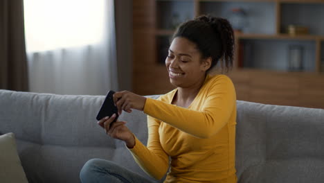 woman smiling while using smartphone on couch