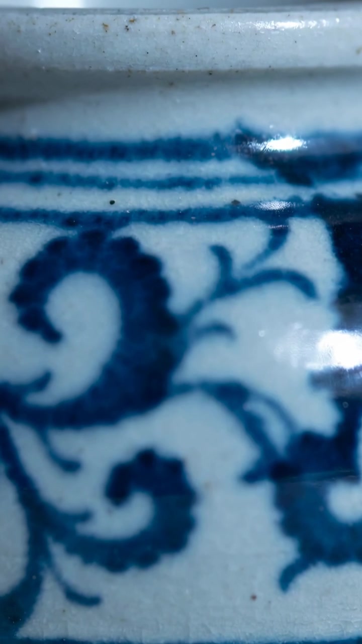 Video verticale: Luce che si sposta creando un riflesso sul bordo di ceramica blu, mostrando macchie di smalto, macro