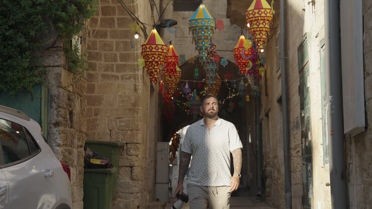 Un uomo con la macchina fotografica cammina verso la luce del sole da un vicolo della città vecchia a Nazareth