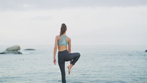 woman practicing yoga by the ocean