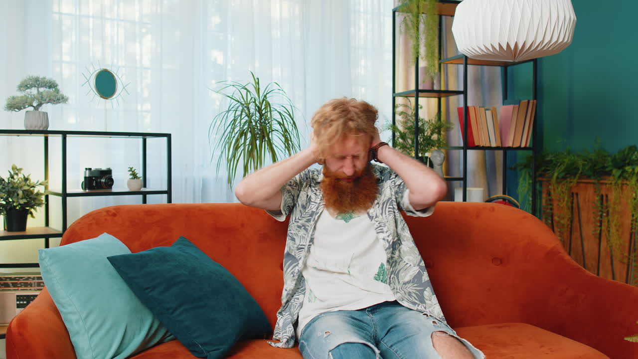 Neighbors repair work, irritated man by loud music at home cover ears with pillows annoyed by noise