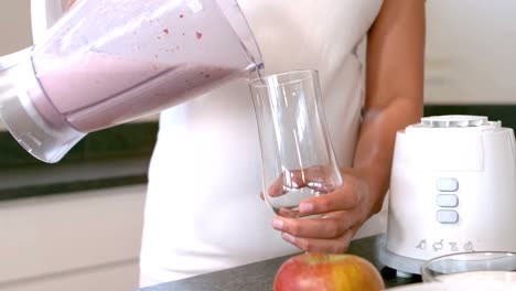 Woman-pouring-smoothie-in-glass-in-kitchen