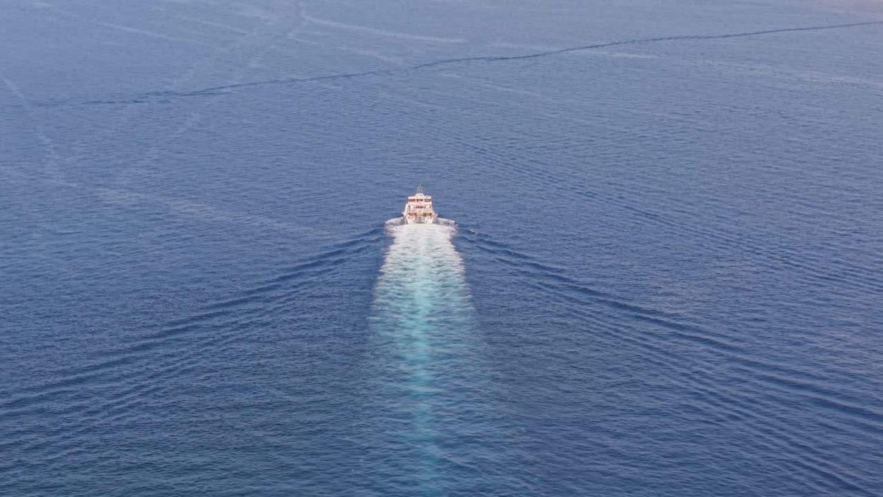 A small boat cruises across the calm open sea, leaving a long foamy white trail behind. The deep blue water stretches endlessly, emphasizing solitude and freedom on the ocean