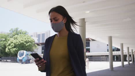 african american woman wearing face mask using smartphone