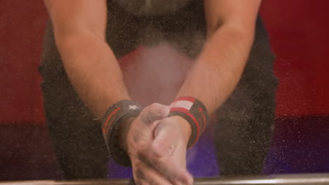 man dusting powder on his hands as he prepares for a workout at the gym