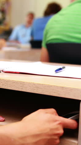 estudiante usando teléfono inteligente debajo del escritorio en clase
