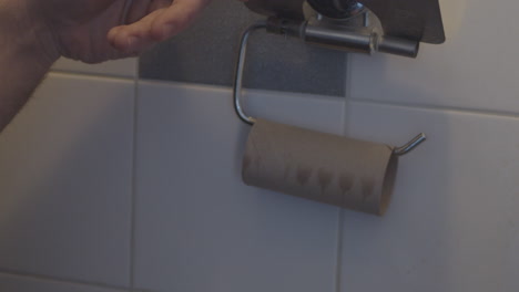 Mano-Agarrando-La-última-Hoja-De-Papel-Higiénico-En-Rollo-En-El-Baño