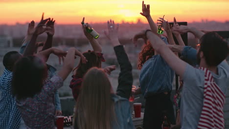 group of friends enjoying a party on a terrace at sunset, hold drinks with arms raised 1