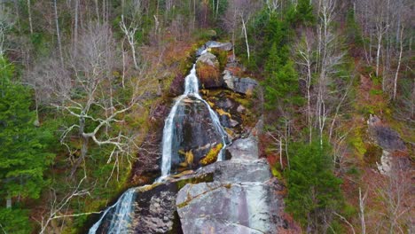 rich landscape with steep waterfall washing down colorful rocks and boulders in the middle of autumn forest