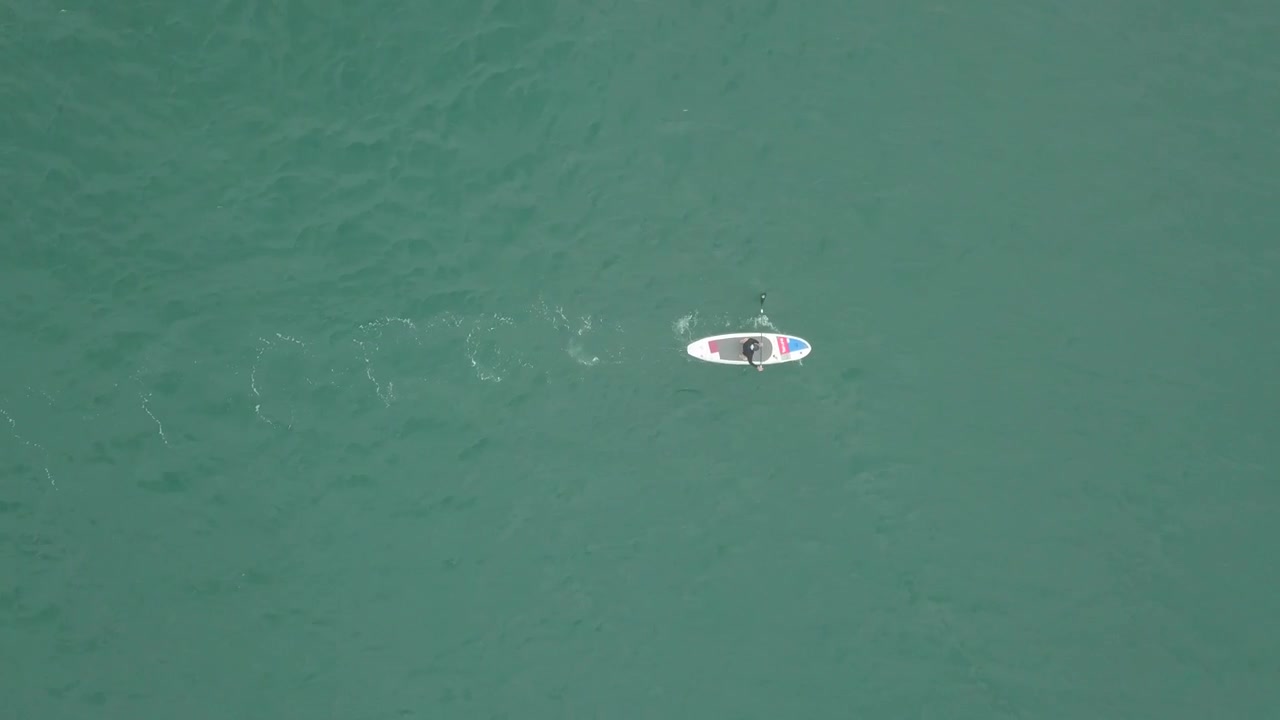 Aerial view with paddleboarder advancing while standing on his board