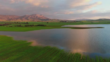 lake surrounded by green fields in greece at sunset with reflections