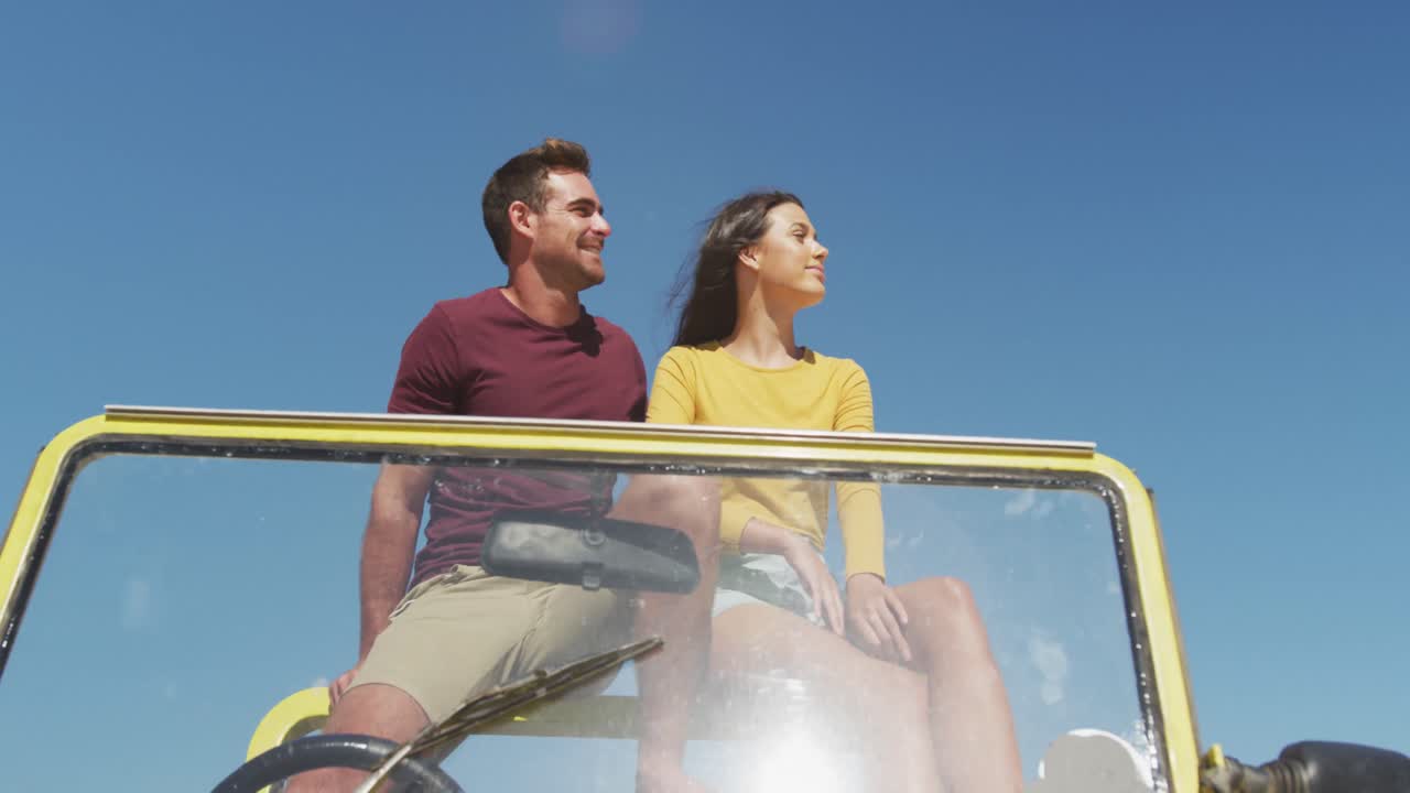 feliz pareja caucásica sentada en un buggy de playa junto al mar hablando