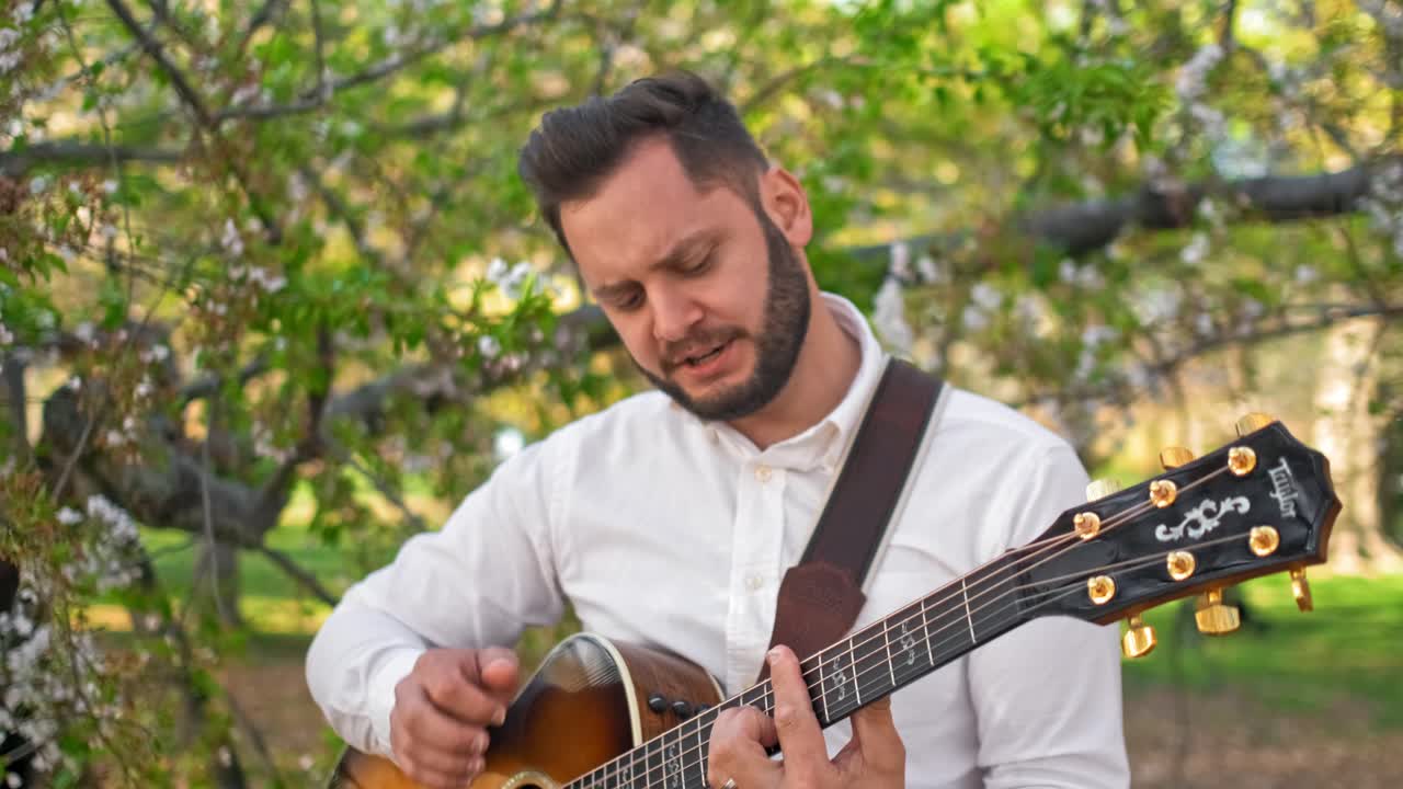 guitarrista tocando su guitarra y cantando al lado de un árbol en un parque
