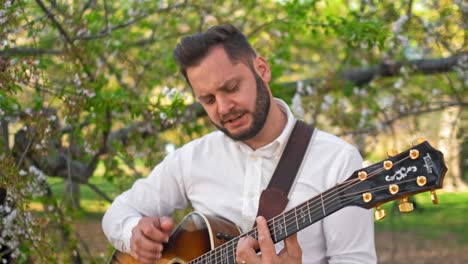 guitarist strumming his guitar and singing next to a tree in a park