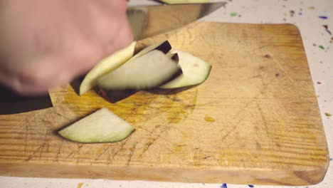 primer plano, las manos cortan rodajas de berenjena con un cuchillo sobre una tabla de cortar de madera