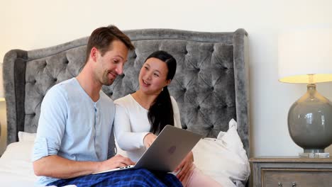 pareja embarazada usando una computadora portátil en la cama en el dormitorio 4k