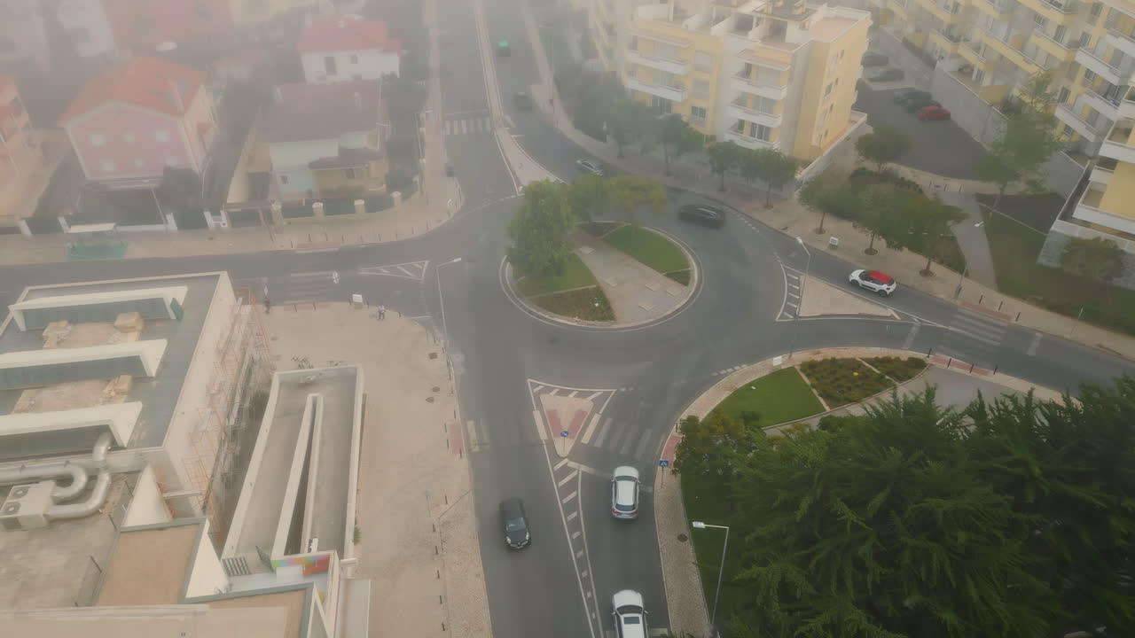 Top small urban roundabout at district covered by autumn mist. Cars riding road
