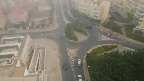 top small urban roundabout at district covered by autumn mist. cars riding road