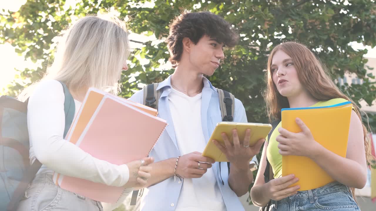 Happy young university students using digital tablet on sunny day