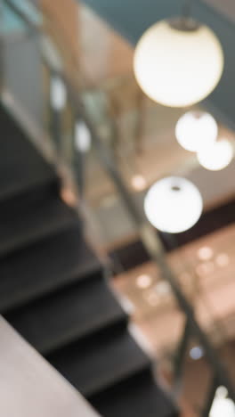 first-person view capturing the staircase with modern glass railings and the surrounding indoor environment. the camera focuses on the sleek design of the stairs and the bright, decorated background